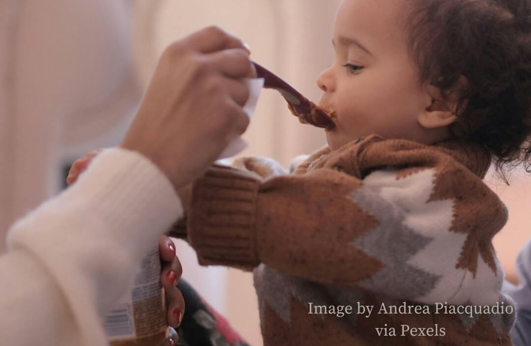 Food before one: baby being fed by spoon