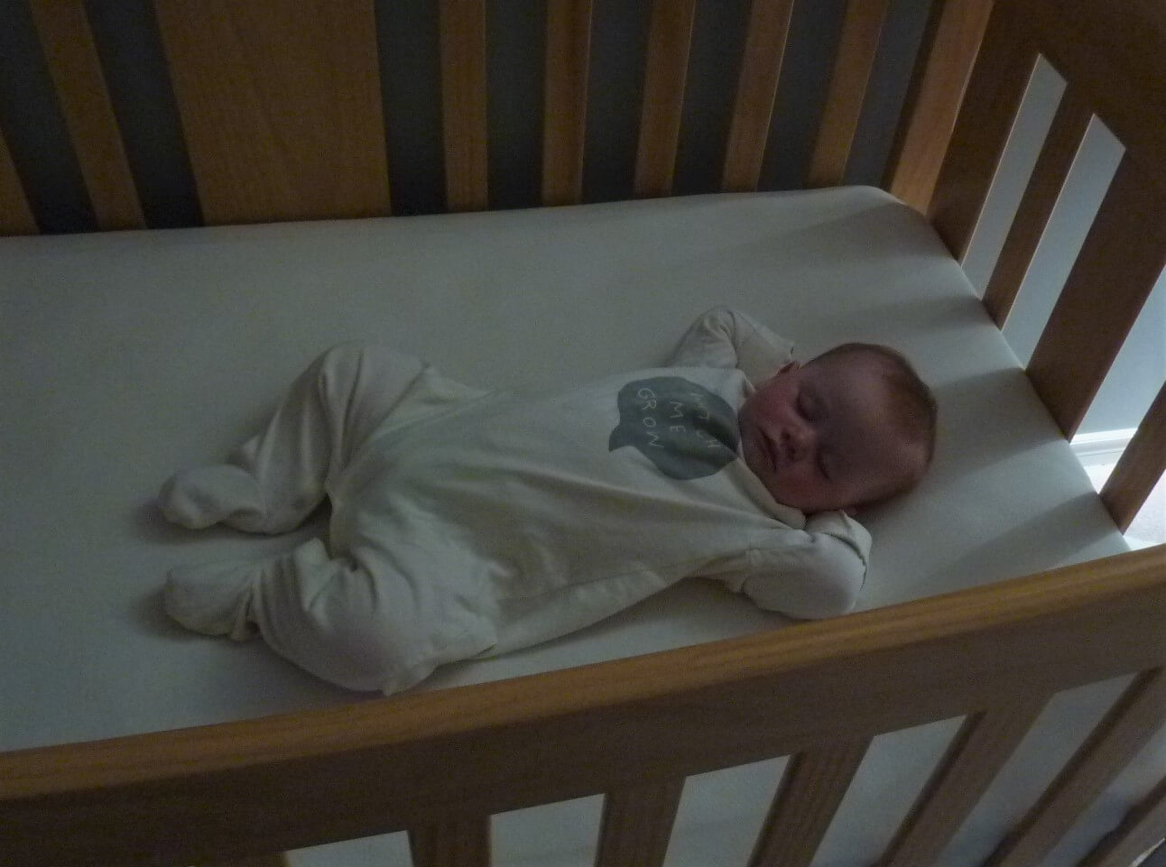 Baby in white footed sleeper sleeping on her back in crib Baby in white footed sleeper sleeping on her back in crib