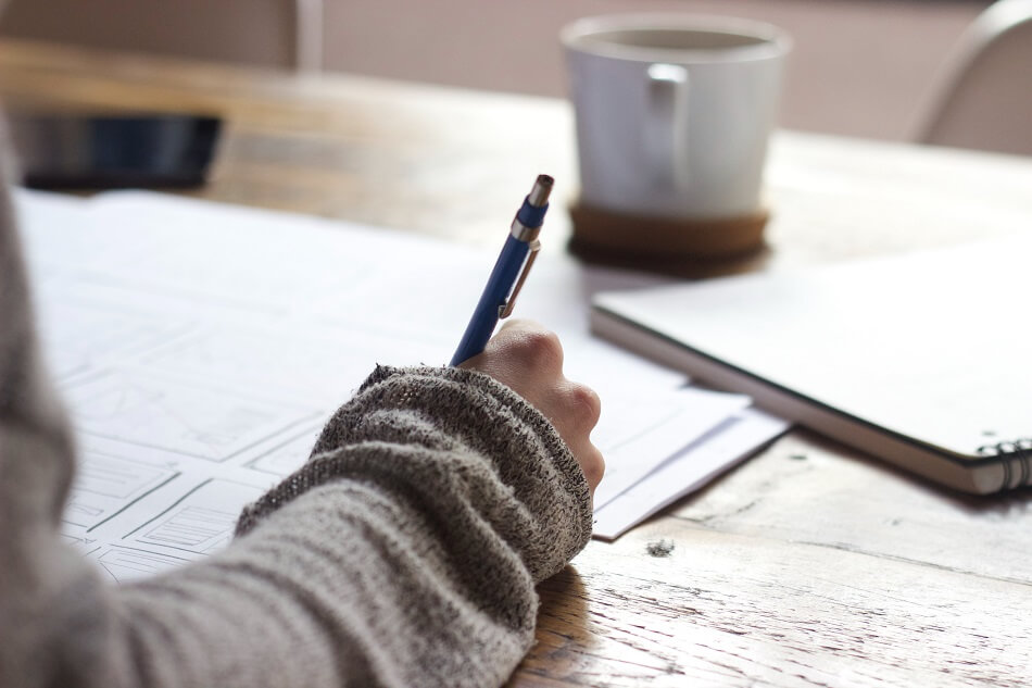 Woman's hand holding a pen and writing, with a cup in the background Woman's hand holding a pen and writing, with a cup in the background