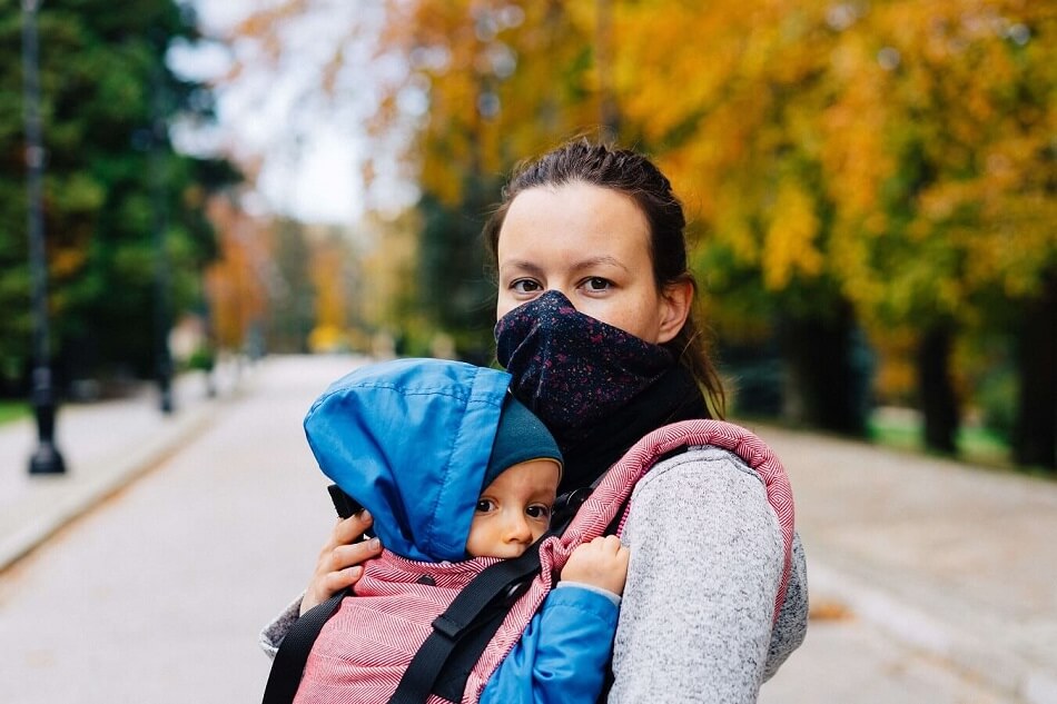 Mother in a mask carrying her baby in baby carrier during Covid-19 pandemic