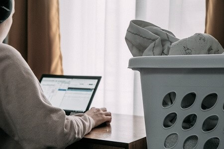 Woman looking at laptop screen with laundry basket beside her Woman looking at laptop screen with laundry basket beside her